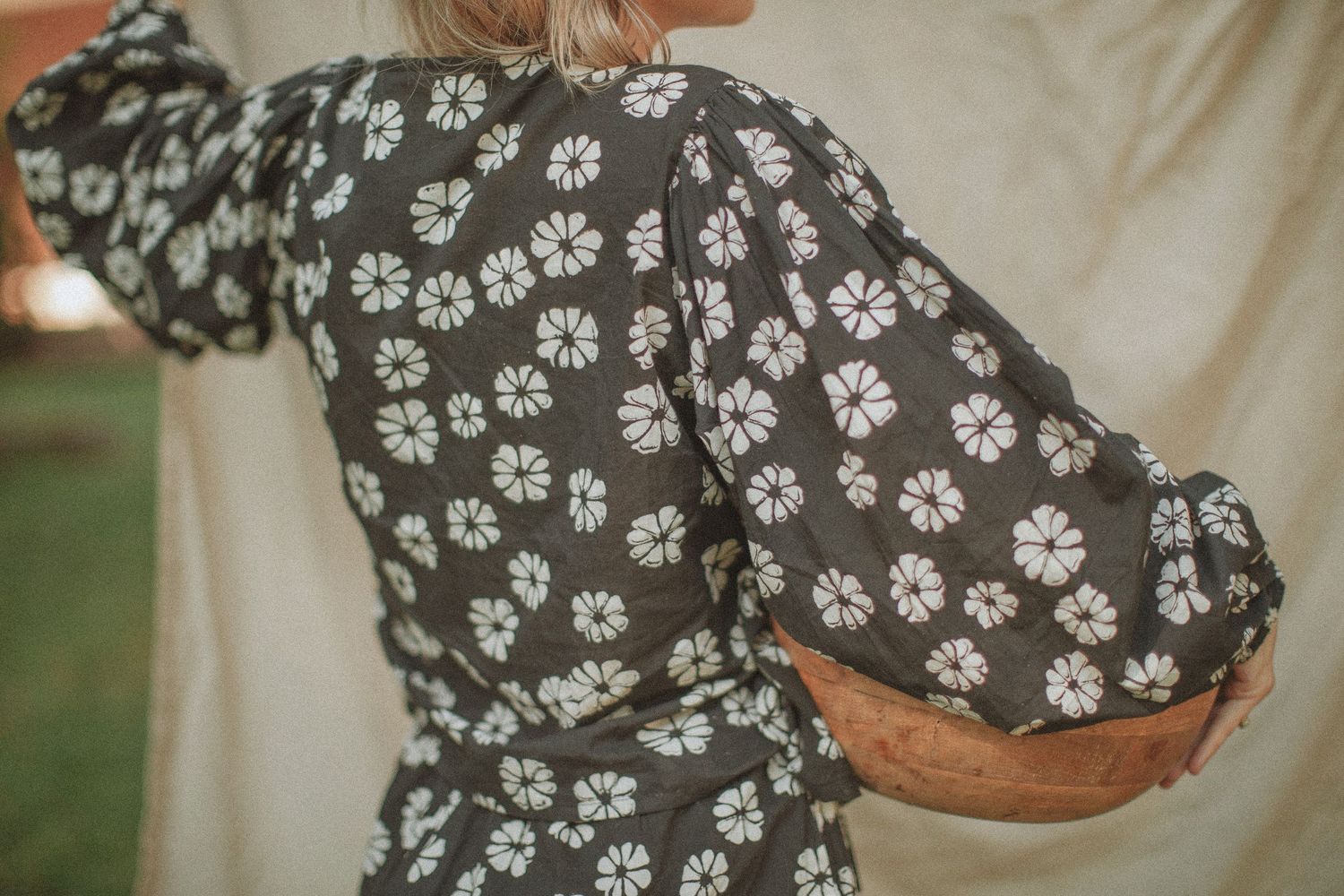 Woman wearing a dark floral print dress with puffed sleeves, holding a woven basket outdoors.