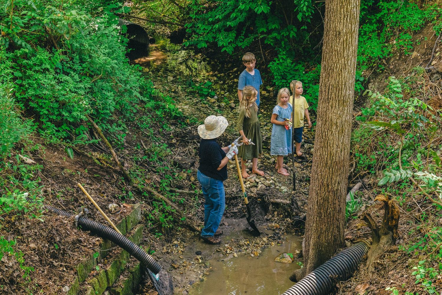 Group of volunteers working near a muddy creek with tools during a nature restoration project.