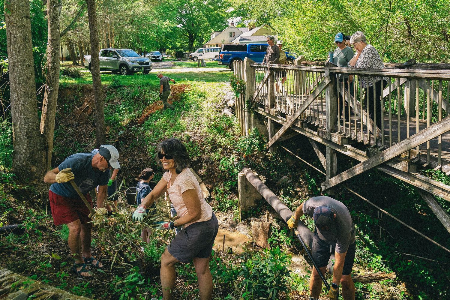 Man in gray shirt using a tool near a creek during an outdoor environmental cleanup event.