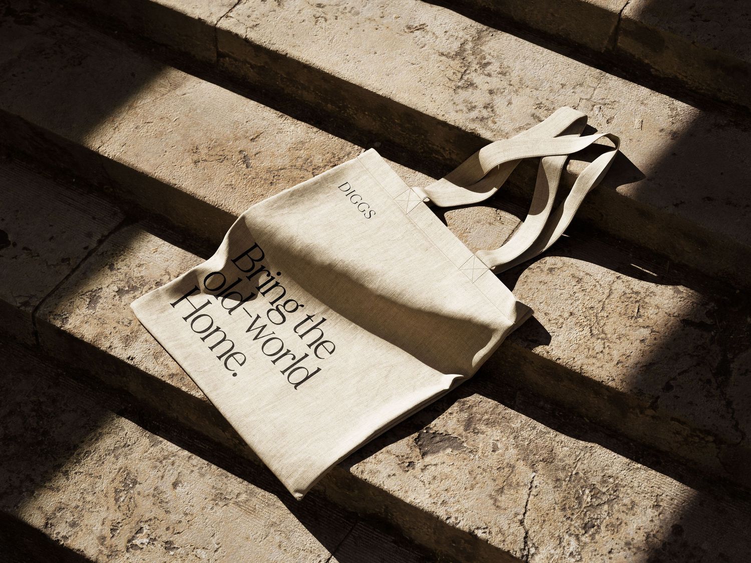 Cream canvas tote bag with 'Bring the World Home' text resting on sunlit stone steps.