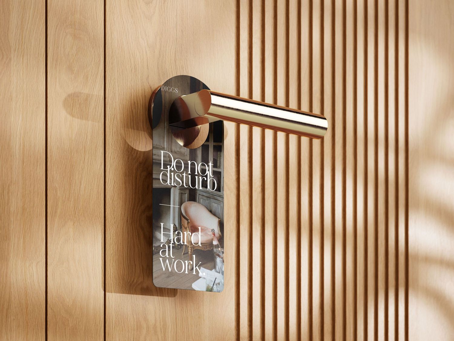 A gold door handle on wooden slat wall with a do not disturb sign reading Hard at Work hanging from it.