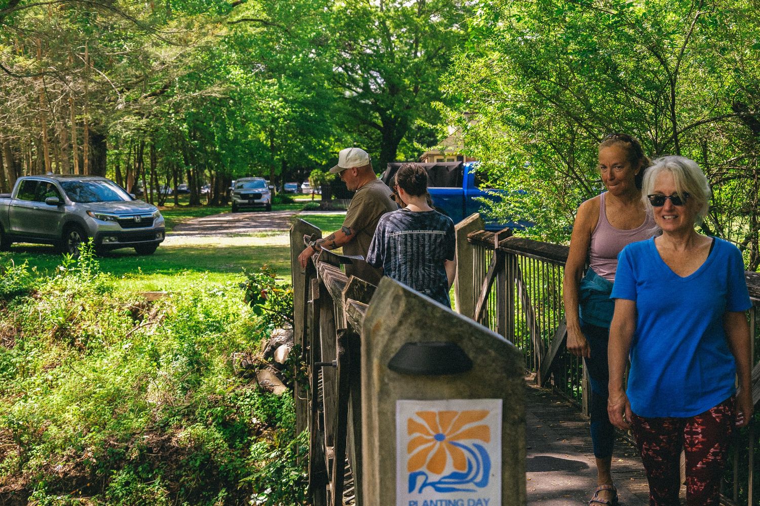 People walking on a wooden bridge trail surrounded by lush green trees in a scenic park.