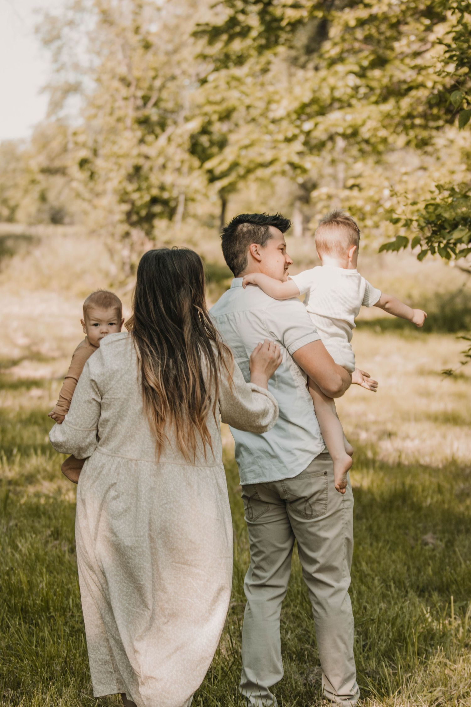 A young family with two babies enjoys an outdoor walk in a lush green park on a sunny day.