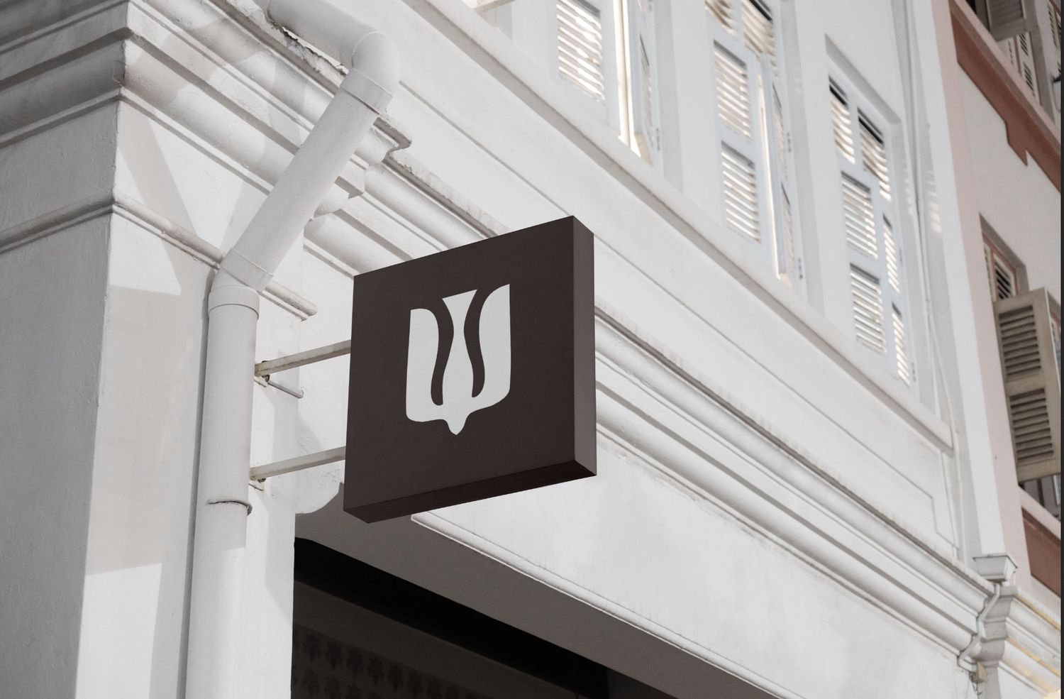 Simple black logo sign mounted on a white building facade with architectural details.