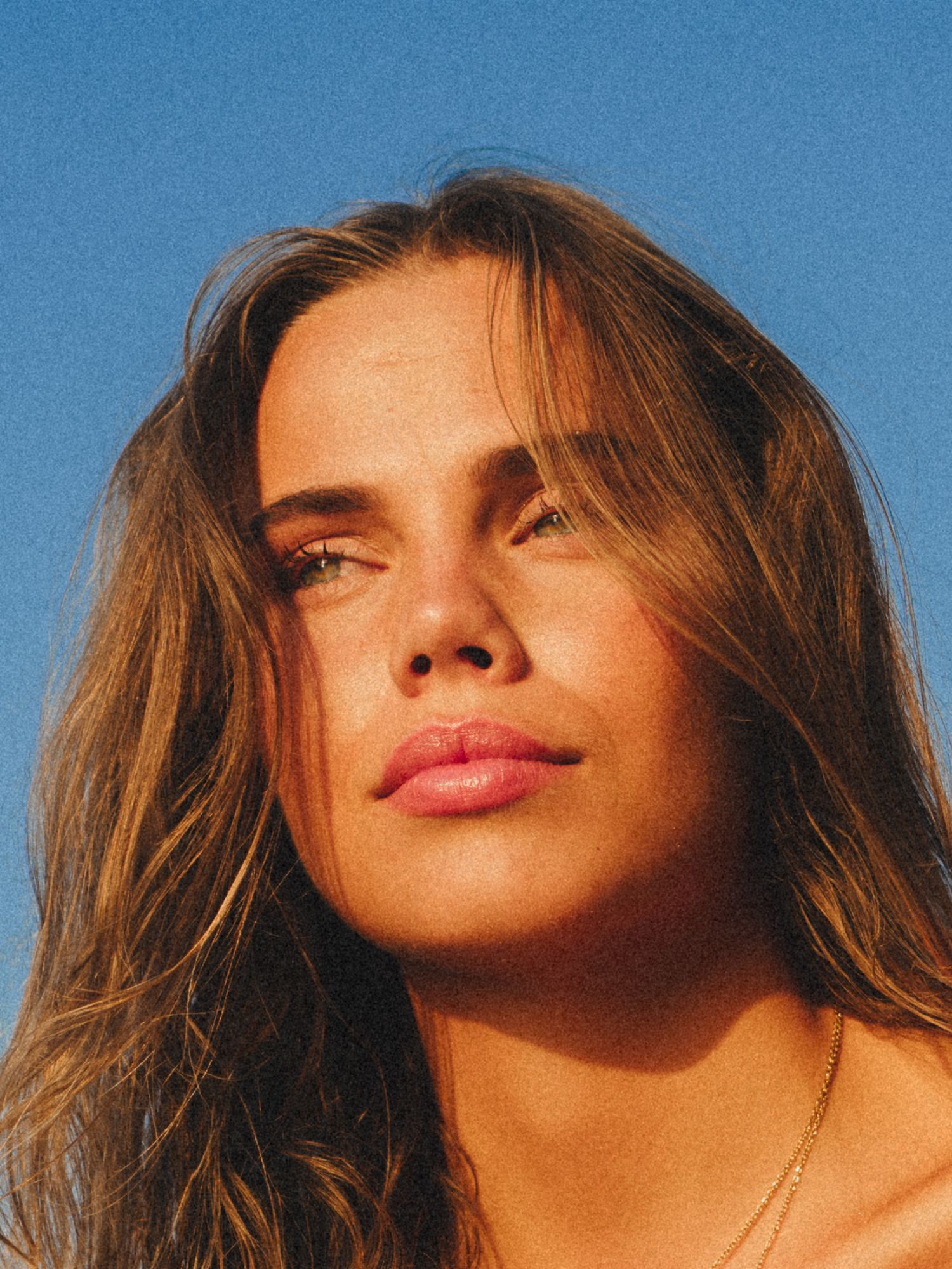 Close-up portrait in golden light showing sun-kissed skin and windswept hair.