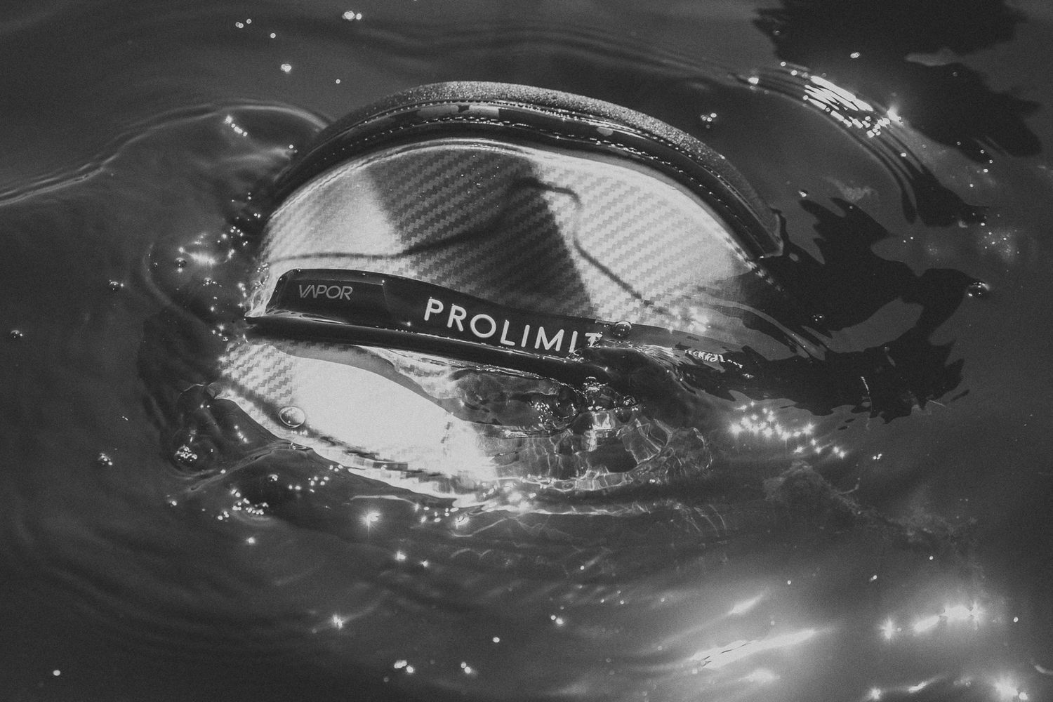 Black and white image of a Prolimit wetsuit hood floating on rippling water surface.