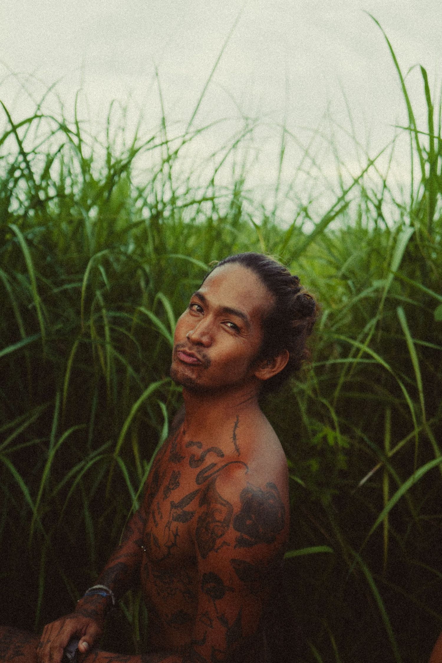 Person with traditional tattoos photographed against a backdrop of tall grass.