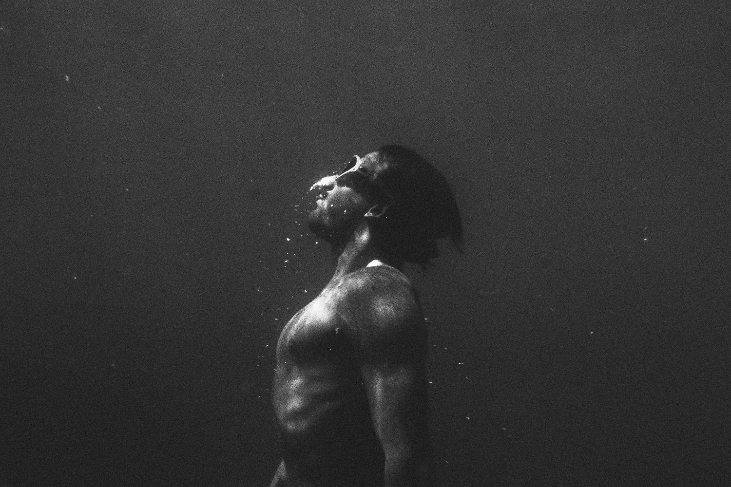 Dramatic black and white underwater portrait of a swimmer emerging from dark waters.