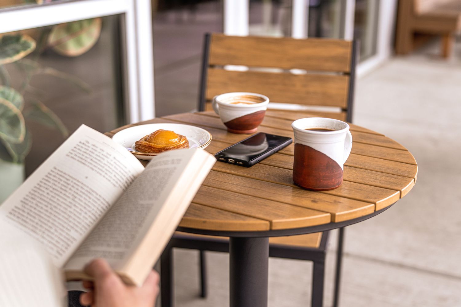 Cozy cafe table with an open book, coffee cup, and phone in natural lighting.