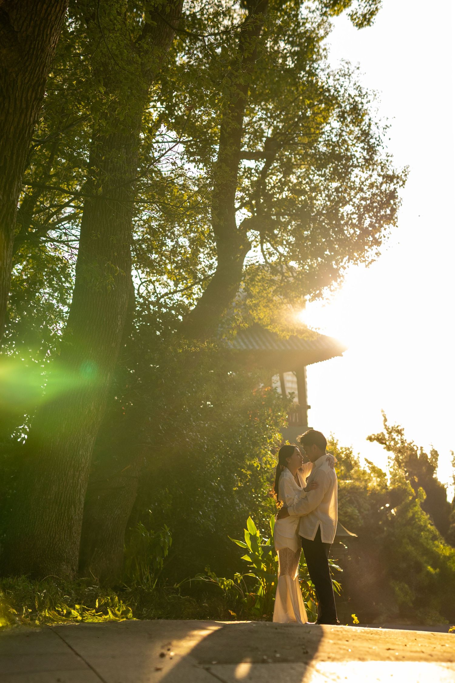 Golden hour photo of a couple sharing an intimate moment near a garden pavilion.
