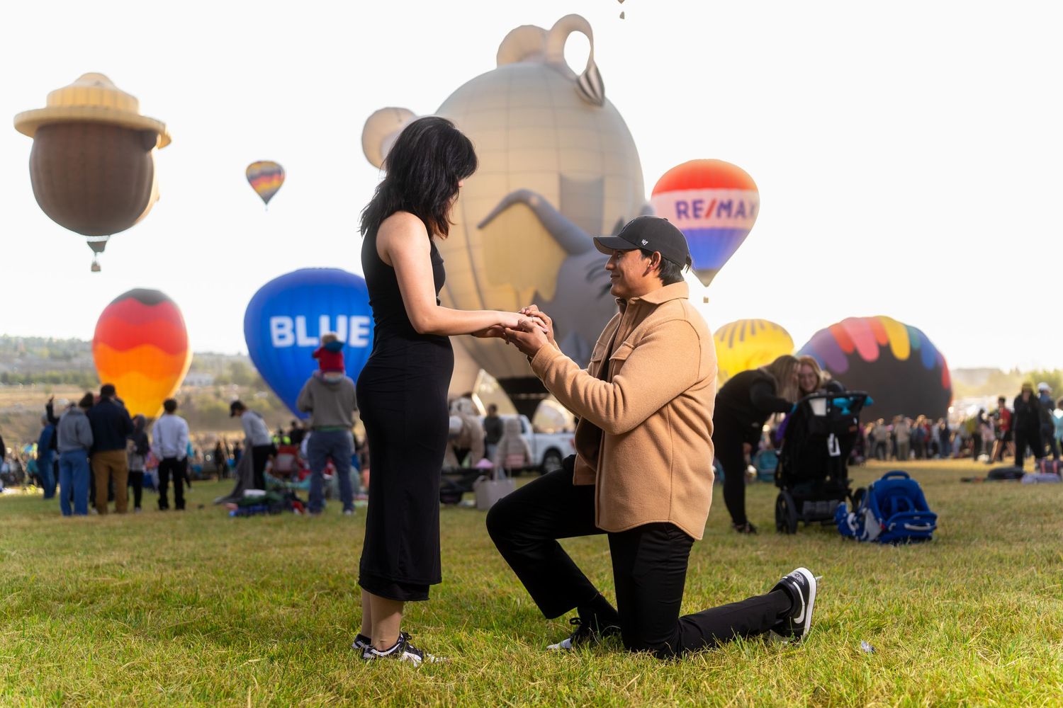 Hot air balloons fill the morning sky at a festival as spectators gather on the grassy field to watch the display.