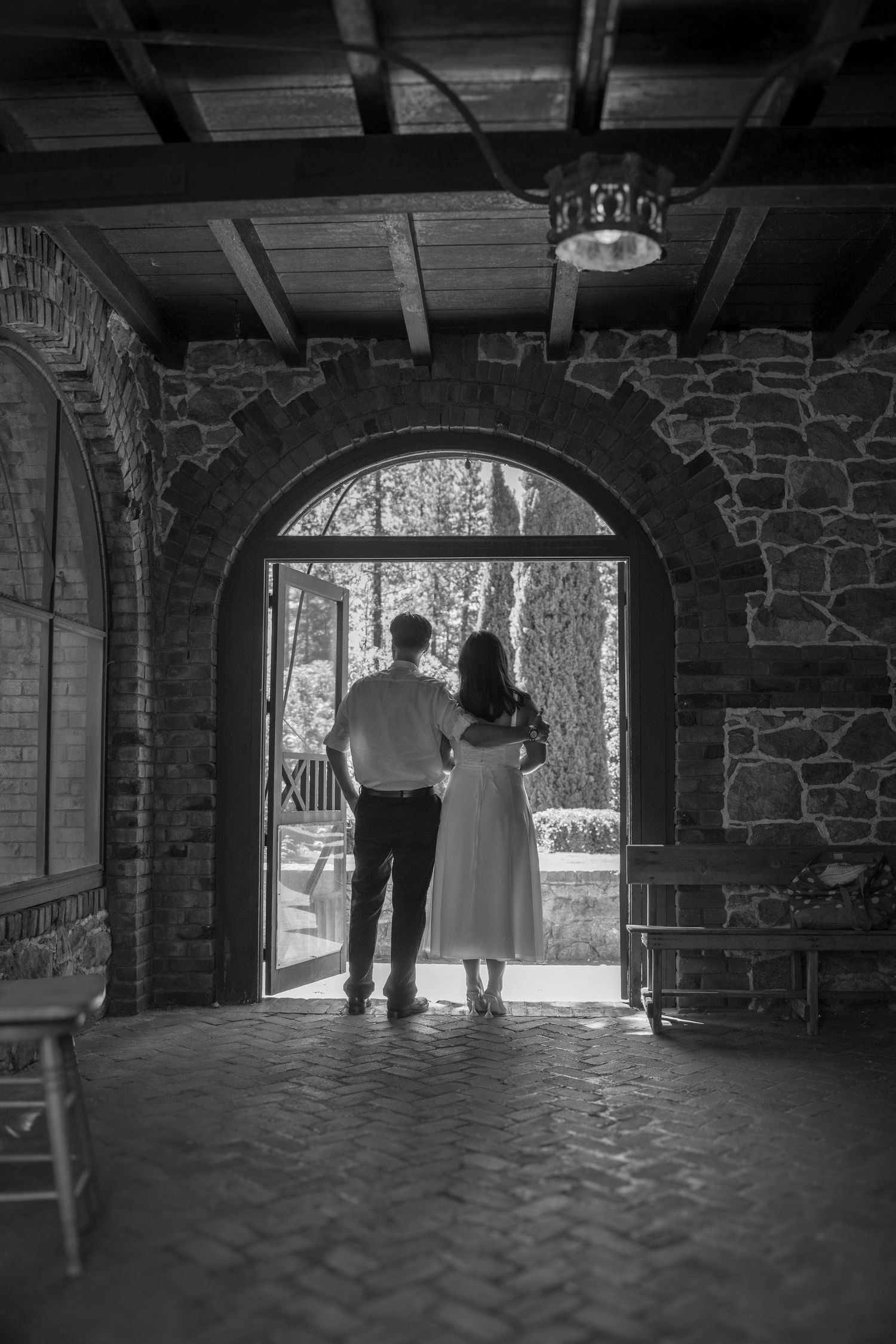 A romantic black and white photo of a couple standing in a stone archway.