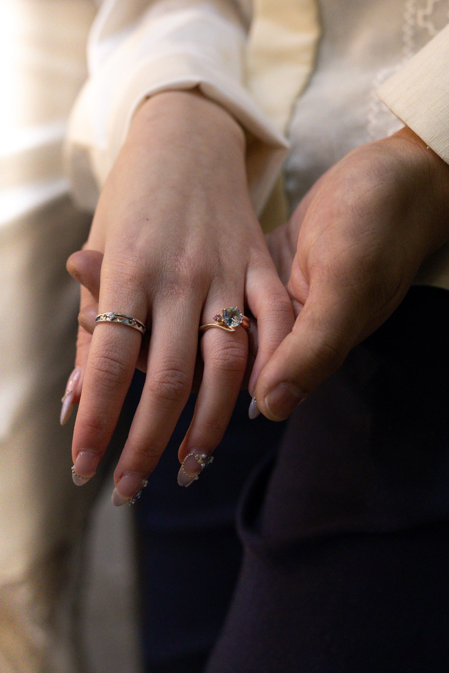 Elegant rings displayed on hands wearing cream-colored sleeves.