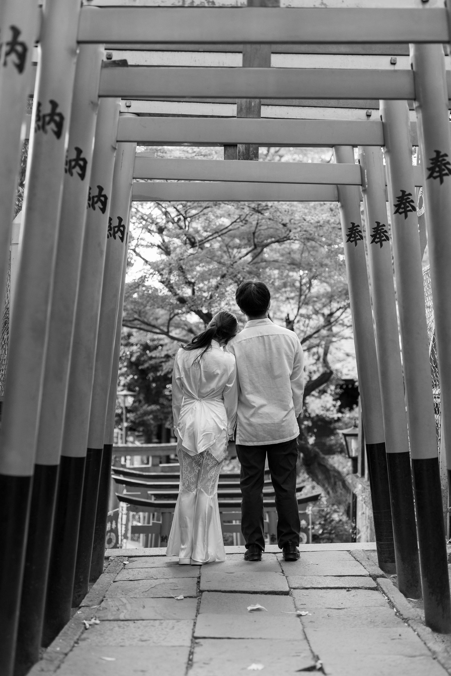 Couple in white clothing standing under traditional Japanese torii gates.