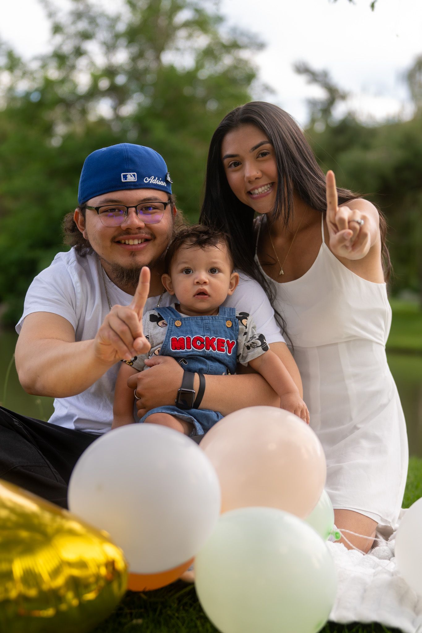Family poses together on grass with colorful balloons during outdoor photo session.