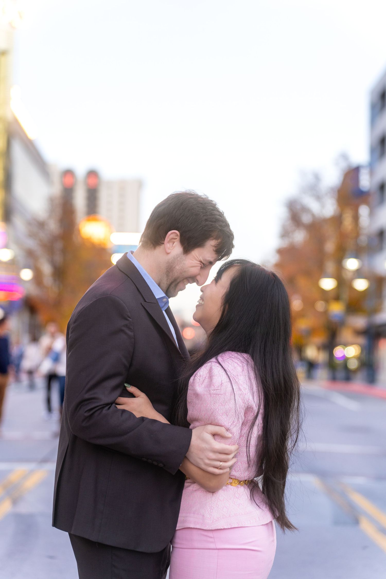 A romantic couple shares tender moments on a city street at dusk while wearing formal attire.