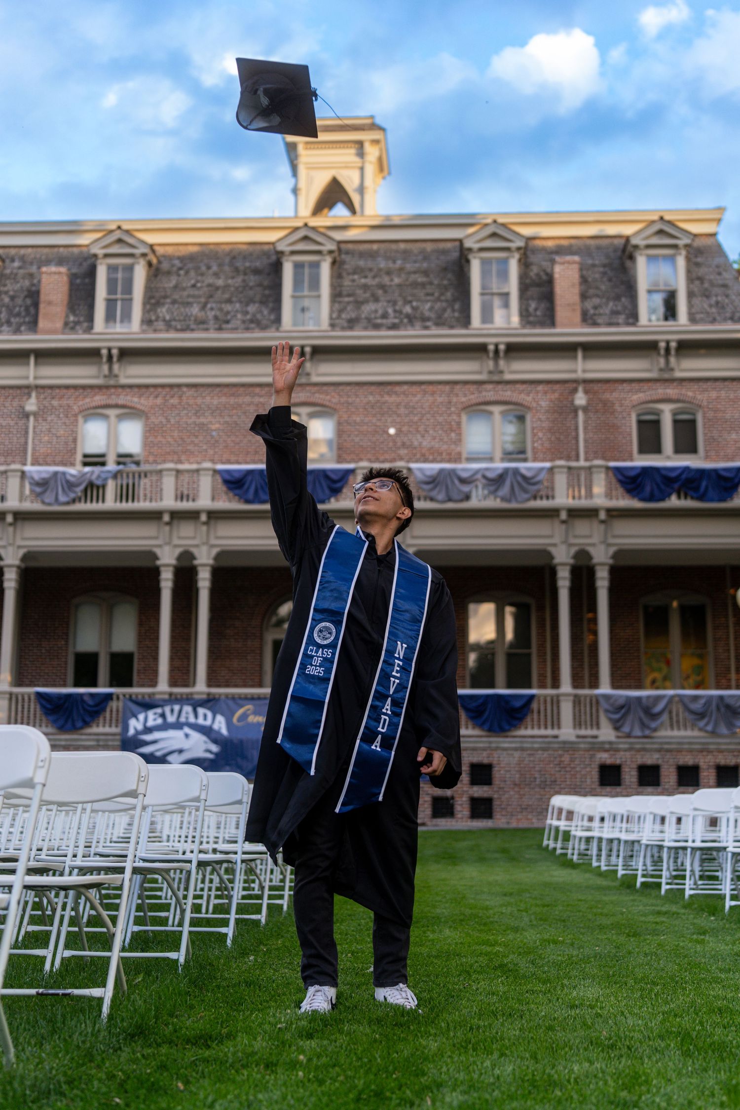 Graduate throwing cap in front of historic building with white chairs set up for ceremony.