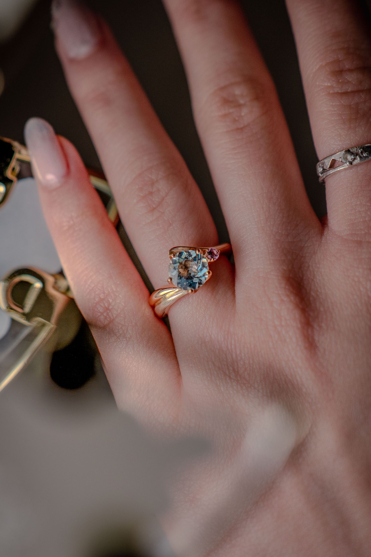 Close-up of a hand wearing two delicate rings, one featuring a blue gemstone.