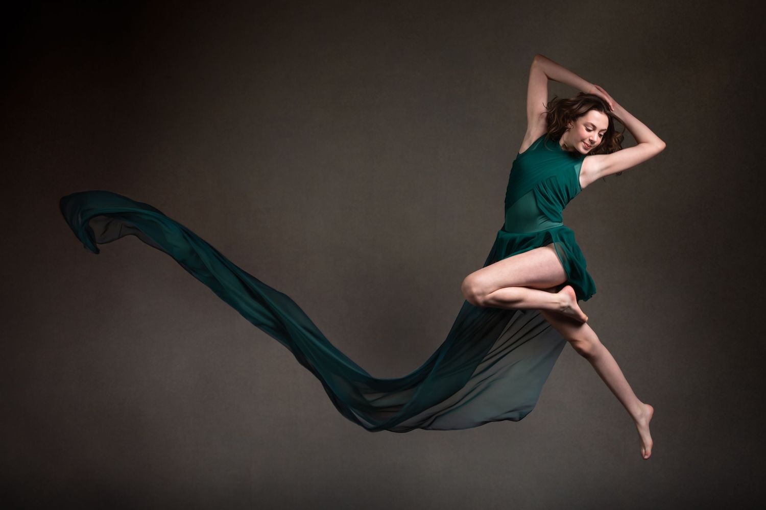 Artistic dance photo with flowing teal fabric creating dramatic movement against dark background.