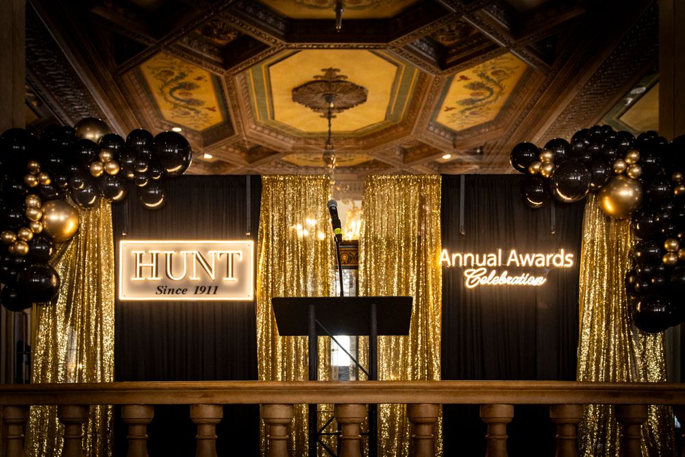 Elegant HUST Annual Awards Celebration stage with gold sequin backdrop, black balloons, and ornate ceiling decor.