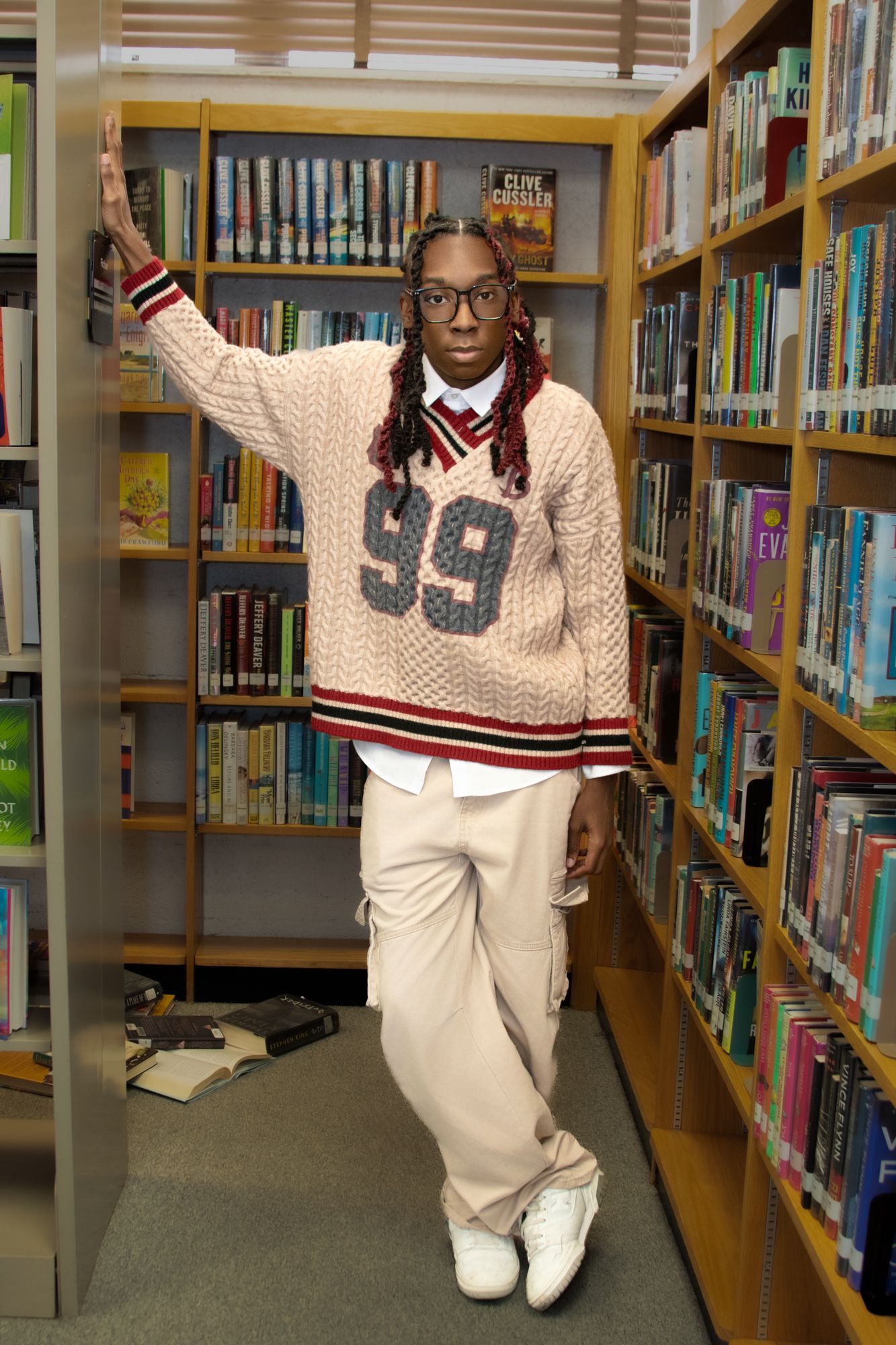 A person wearing a varsity sweater and white pants poses in different playful stances between library bookshelves.
