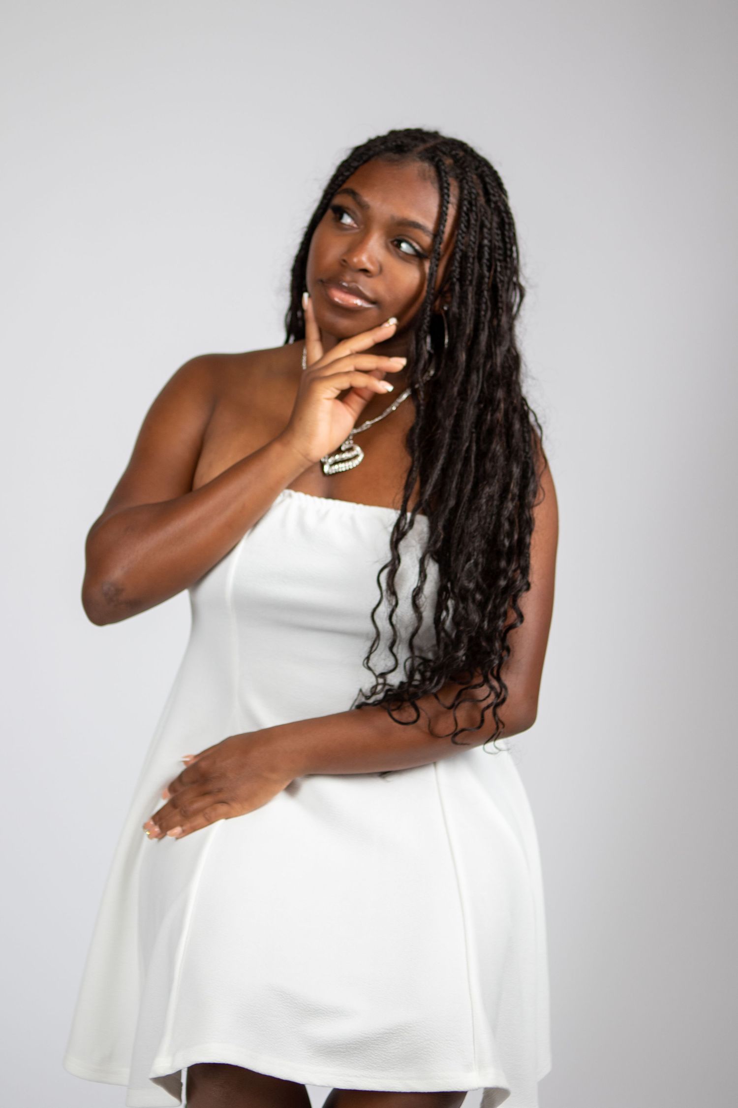 Elegant portrait in white dress with long braids against grey backdrop.
