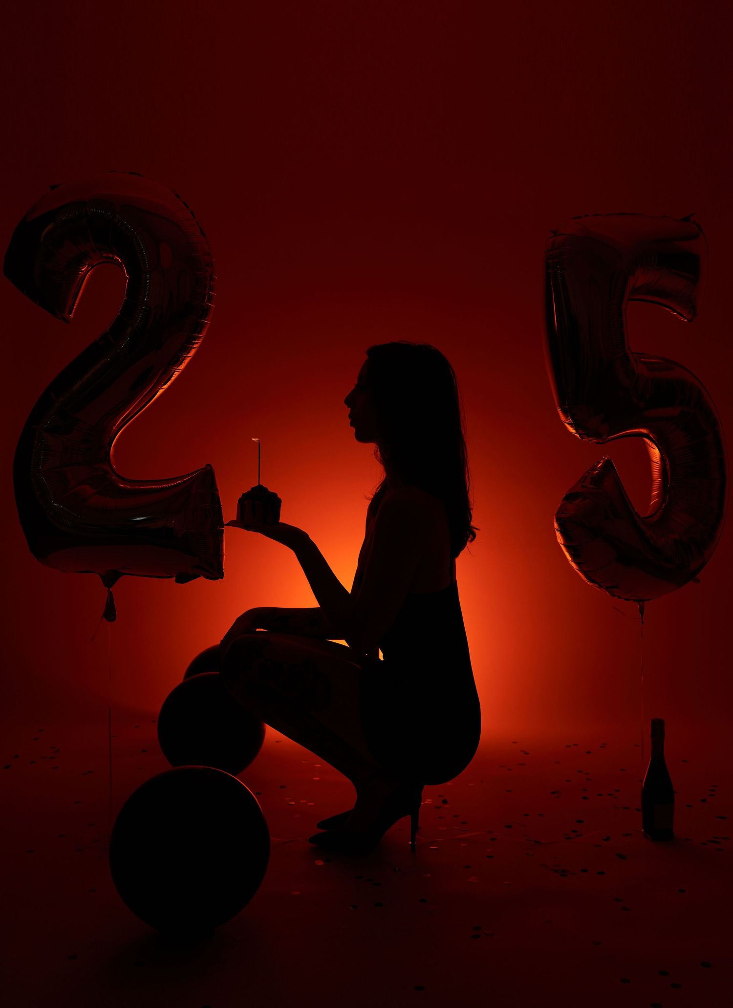 Silhouette of woman posing between number 25 balloons in dramatic red lighting for birthday.