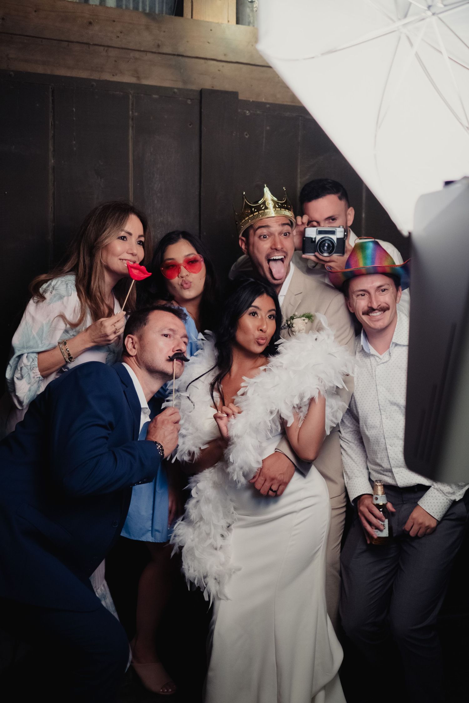 Wedding party posing in photo booth with fun props including feather boa, crown, mustaches, and colorful glasses at a San Francisco wedding.