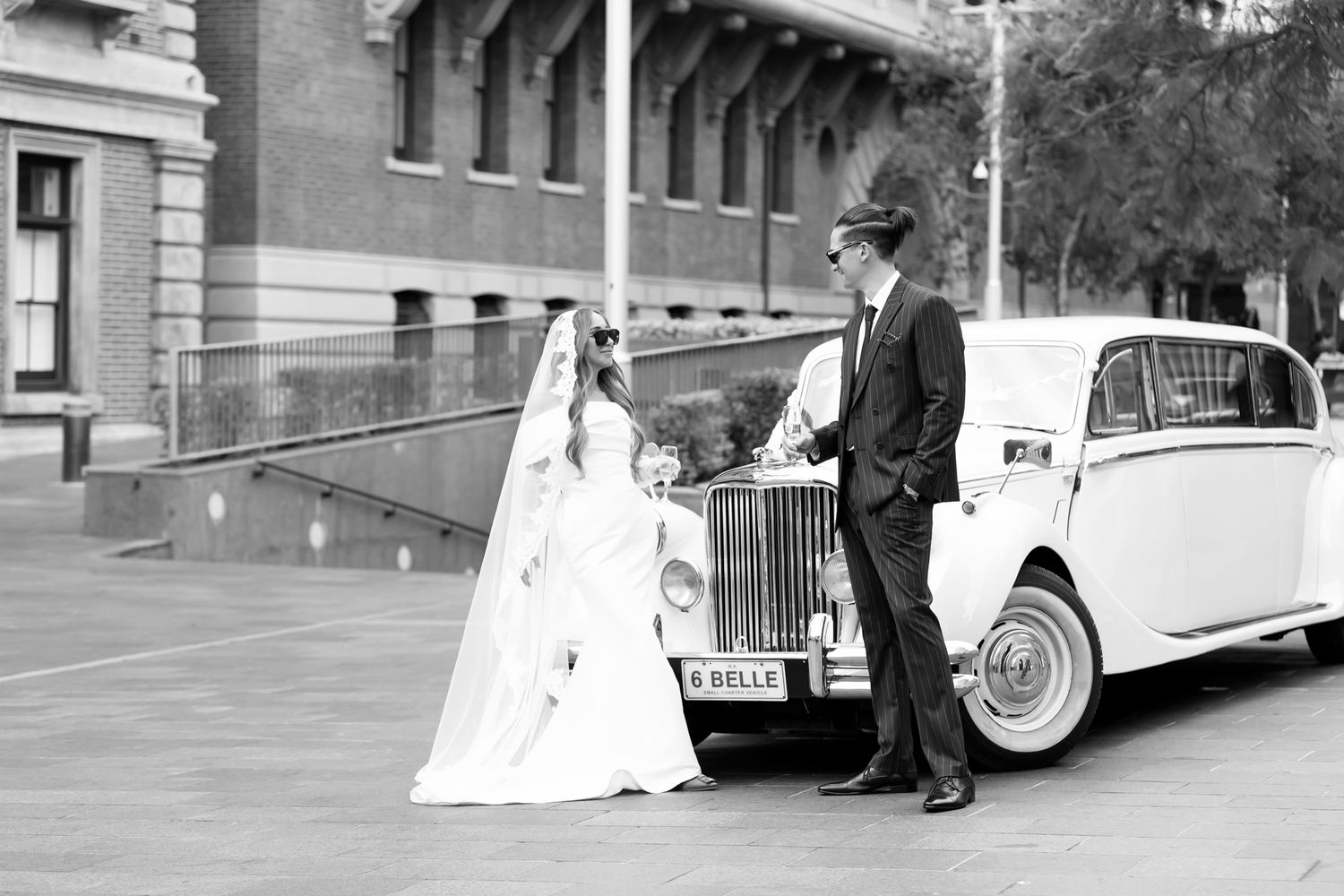 Black and white photo of a bride and groom posing beside a vintage Rolls-Royce on their wedding day.