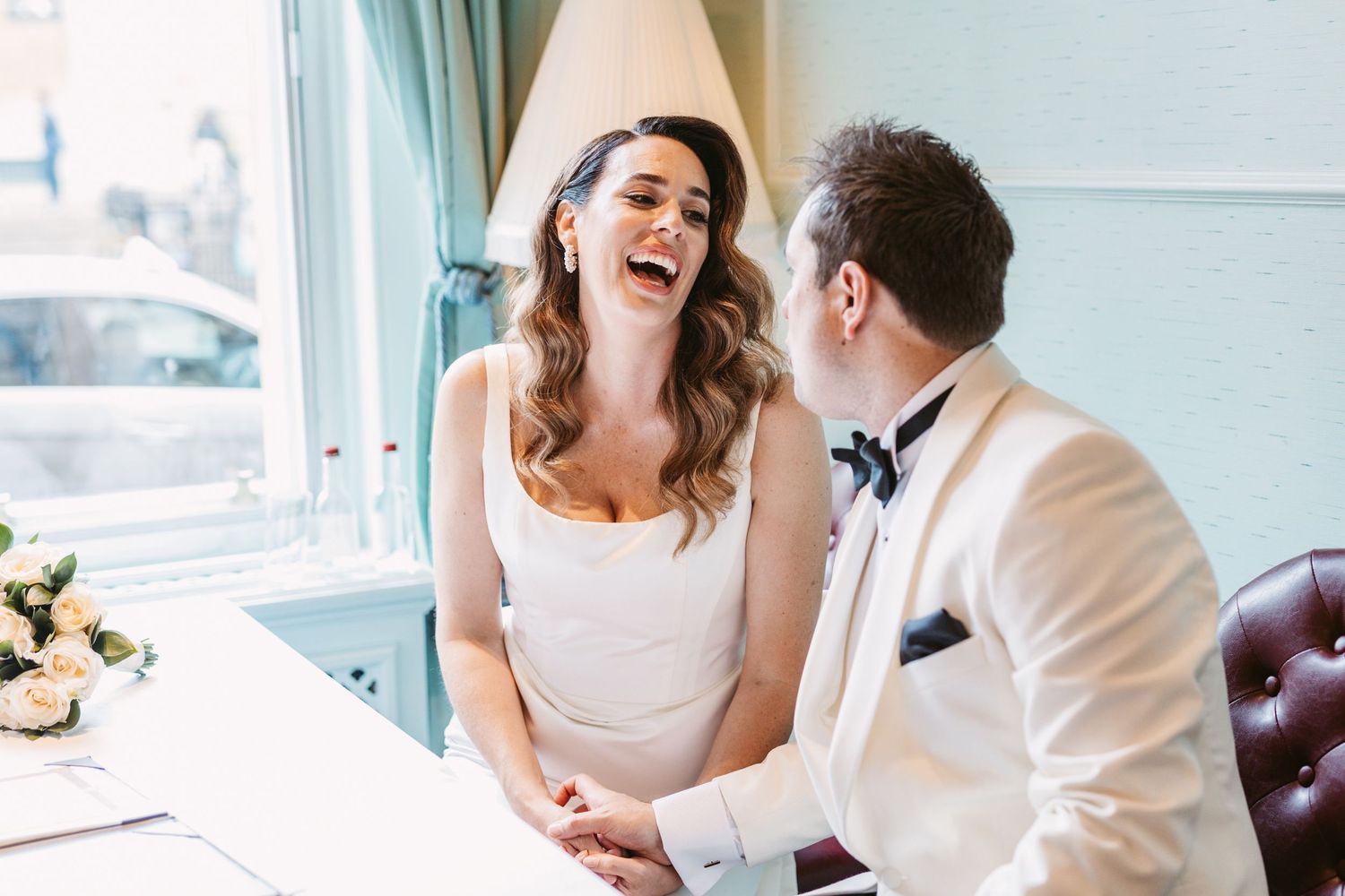 A joyful moment shared in an elegant room with natural light streaming through windows at The Randolph Hotel, Oxford.