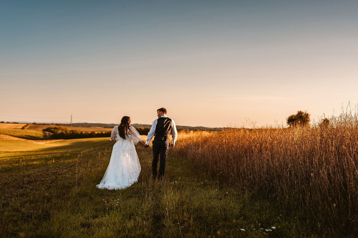 A couple celebrates their wedding at golden hour in a field with tall grass and a warm sunset sky Luxury wedding package for modern couples