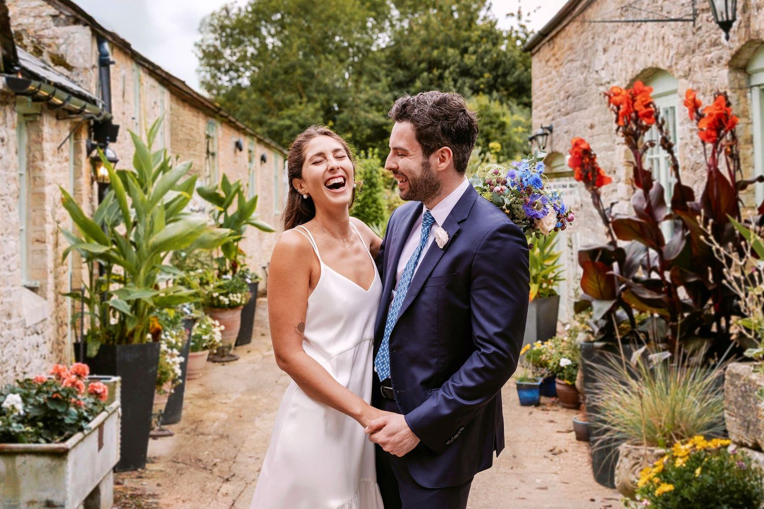 Wedding celebration at a rustic stone venue with vibrant orange and red floral decorations. Bride and Groom laughing affectionately together