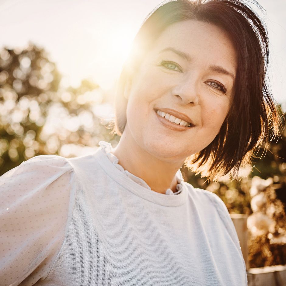 Smiling person in white sweater photographed at golden hour with sunlit bokeh background.