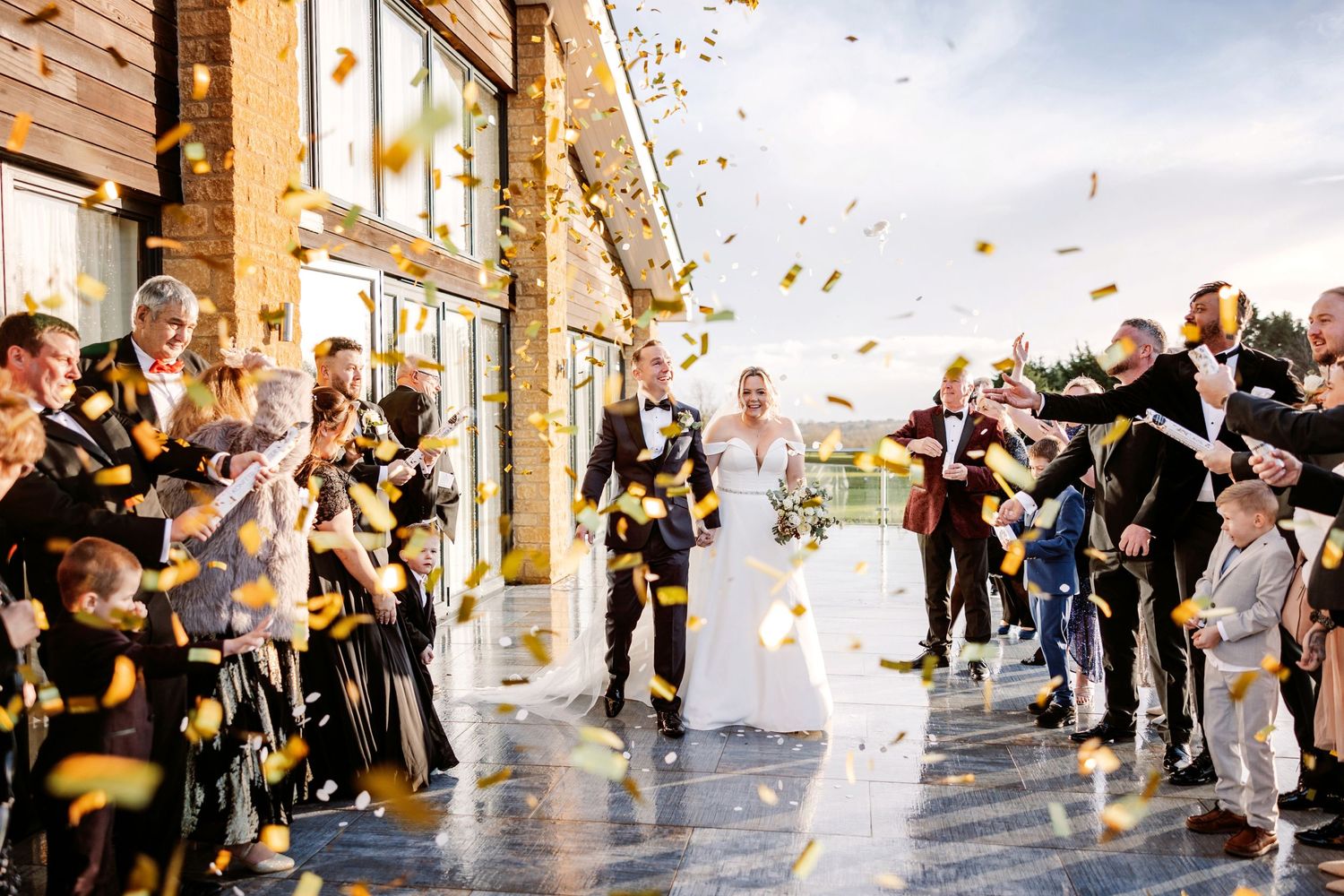 Wedding celebration with guests showering newlyweds in flower petals and confetti outside elegant venue Cotswold Hotel and Spa.