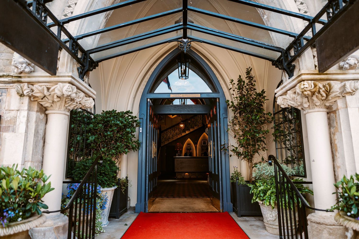 A grand entrance with a red carpet leading to ornate Gothic-style archway with potted plants.