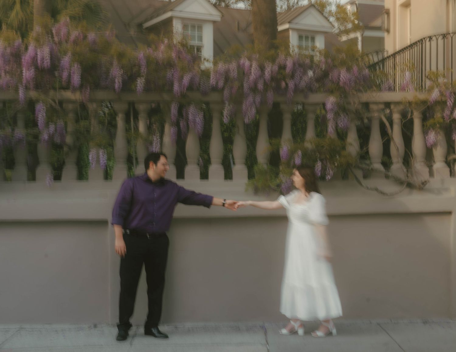 A couple dances together under blooming wisteria flowers on an outdoor patio during a wedding celebration.