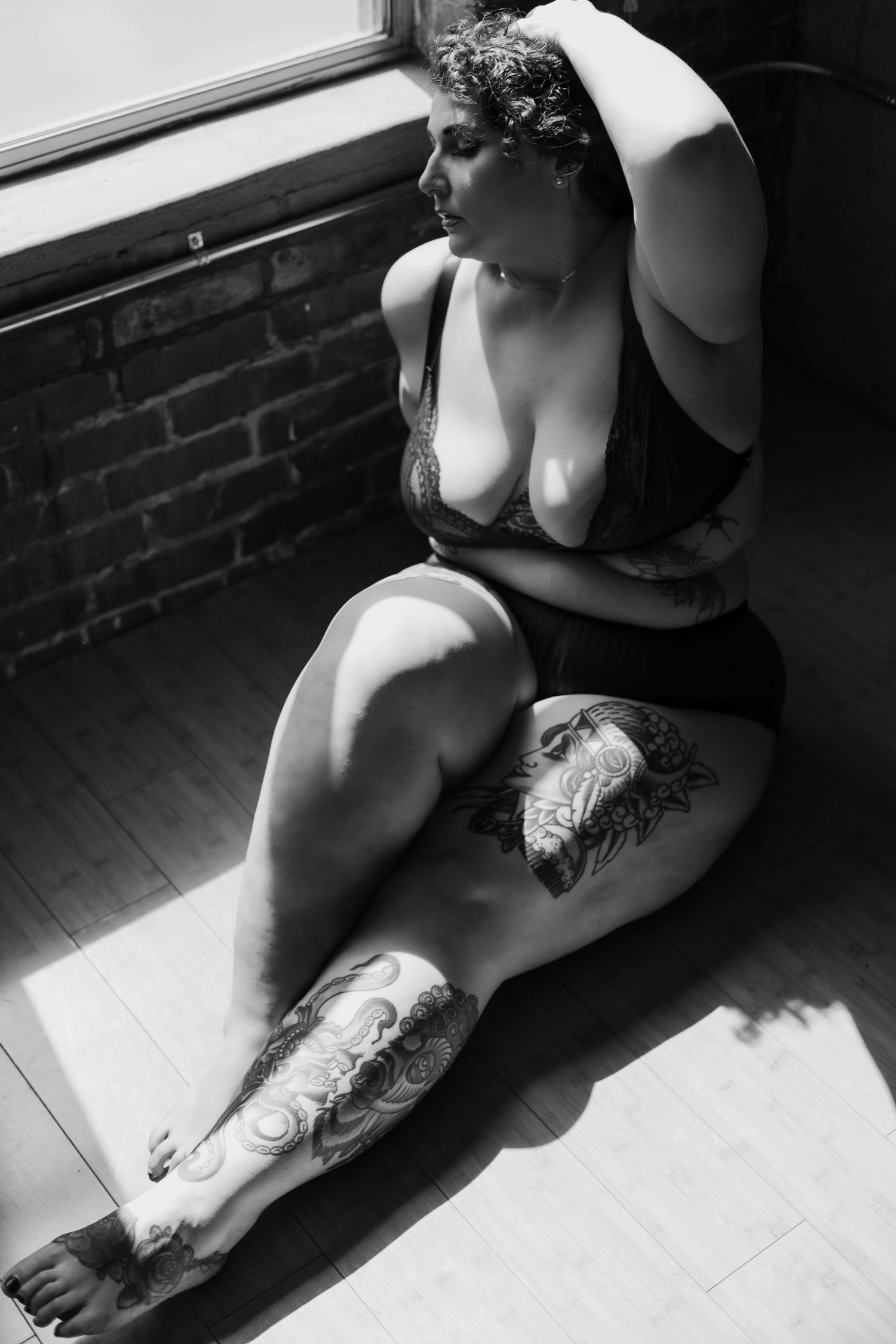 black and white image of a woman wearing lingerie, running her hand through her curly hair