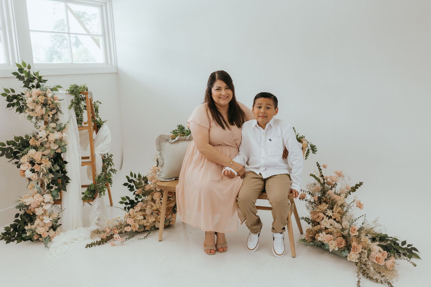 floral setting with wood bench, woman and young child sitting on bench smiling at the camera.
