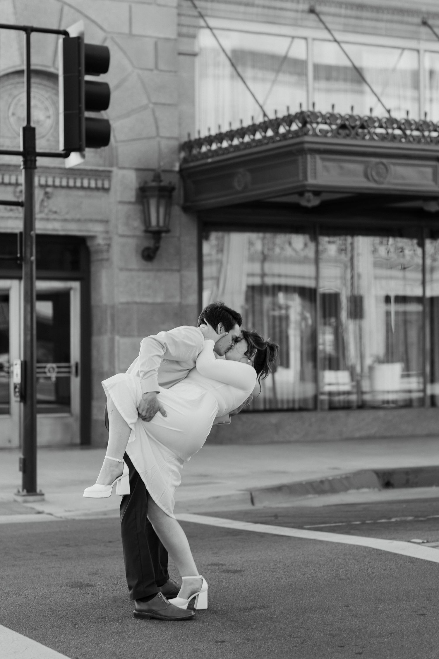 couple kissing in a city crosswalk, one partner dipping the other. with a historic grand 1401 building in the background.