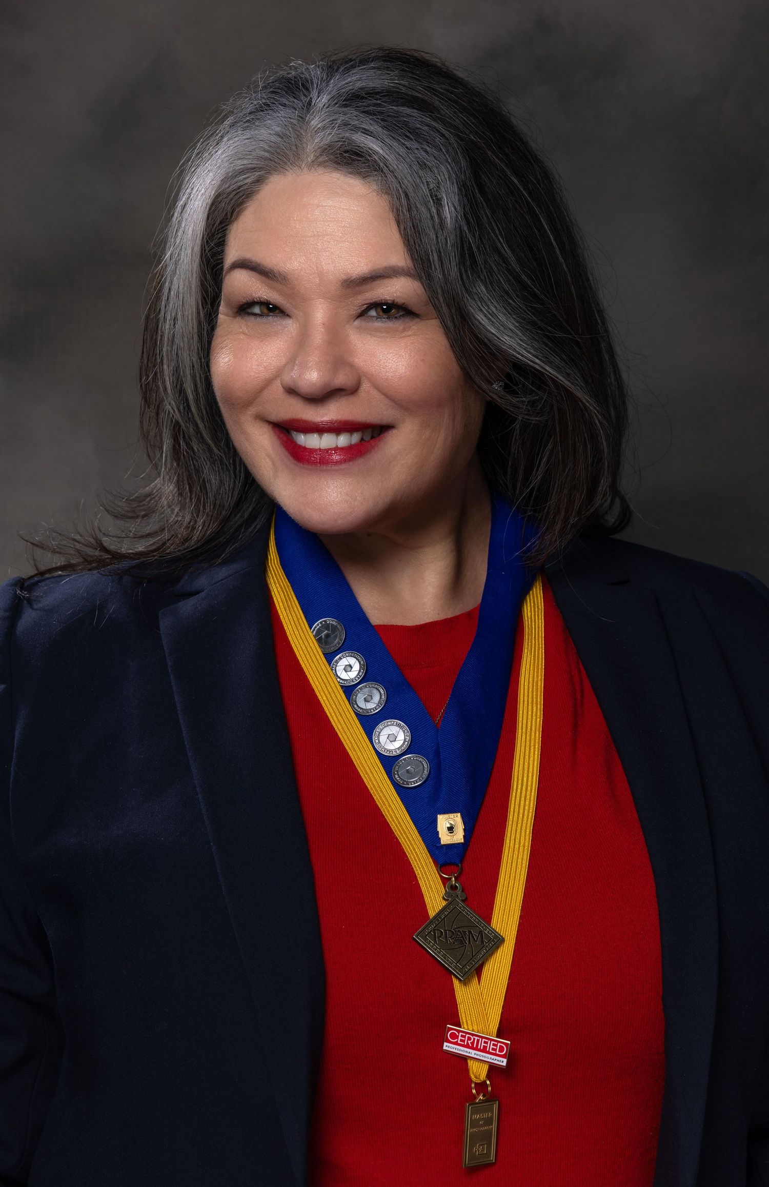 A person in a navy blazer and red sweater with yellow sash and medals poses in a series of professional headshots.