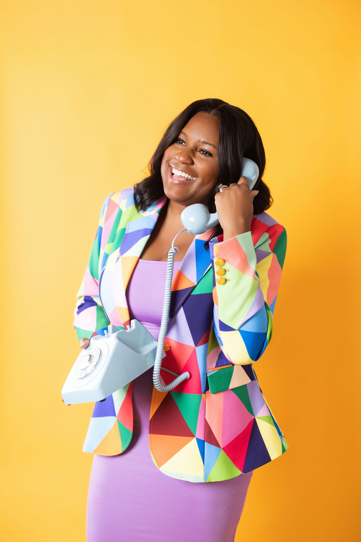 Four dynamic poses against a vibrant orange background showcase a colorful geometric print jacket and purple dress.