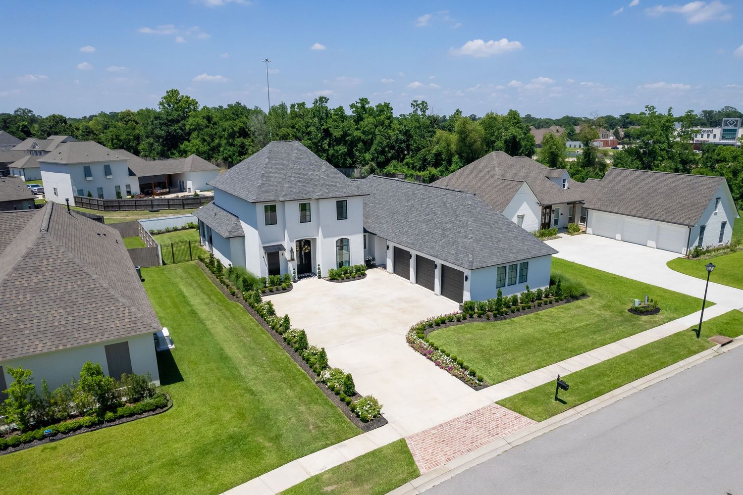 Aerial drone view of residential neighborhood with green lawns and gray roofed houses on a sunny day.