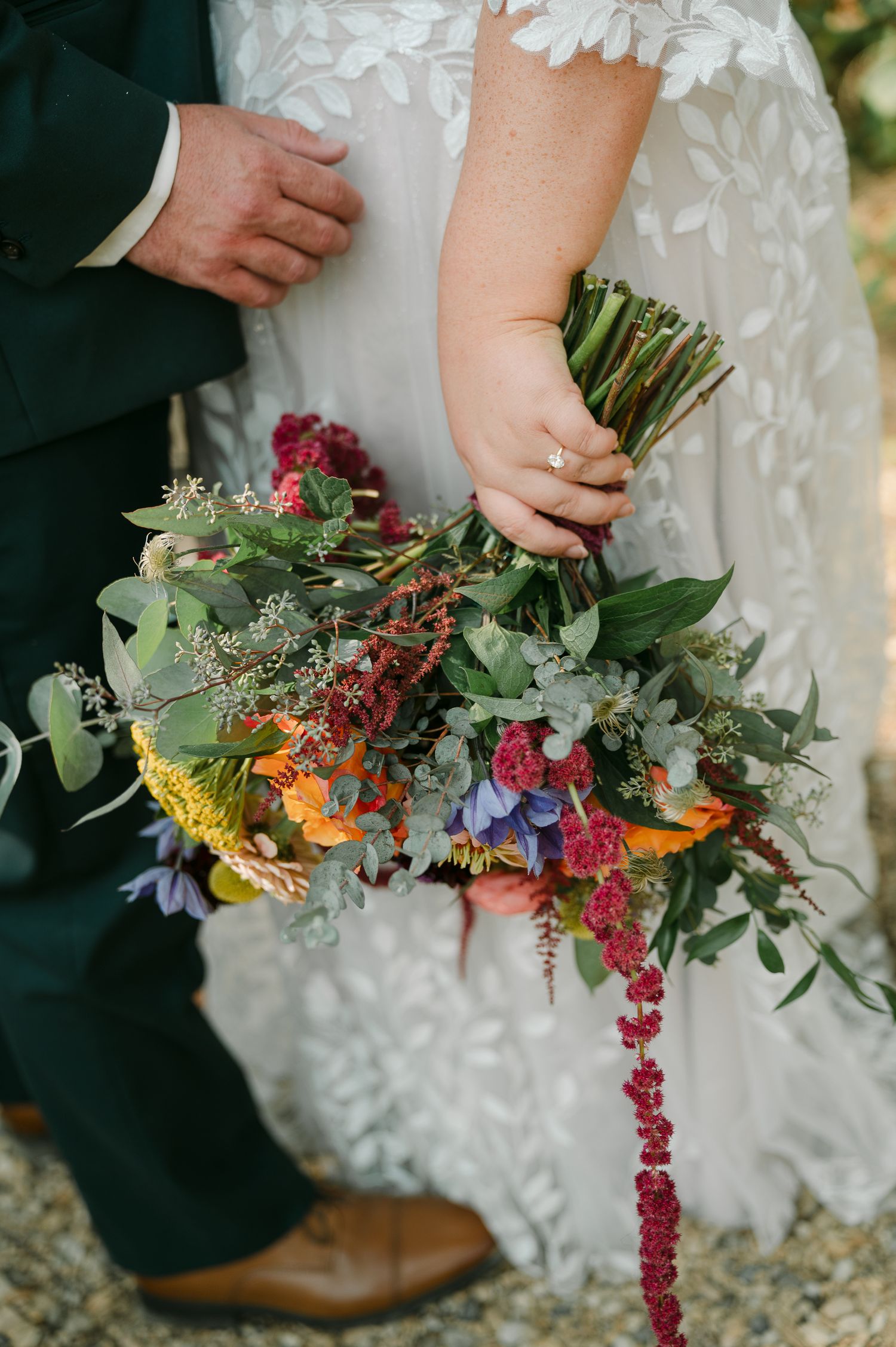 Bride holding a lush, colorful wedding bouquet with orange, purple, and red blooms with trailing amaranthus.