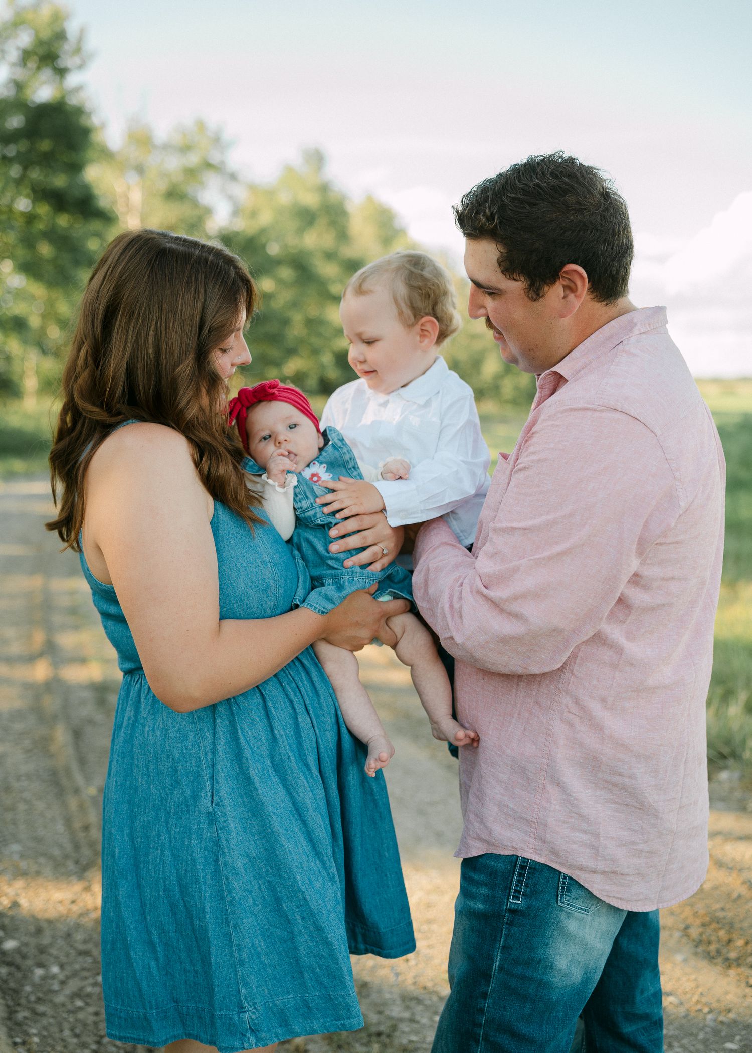 Family of four with two babies facing each other on a dirt road at golden hour.