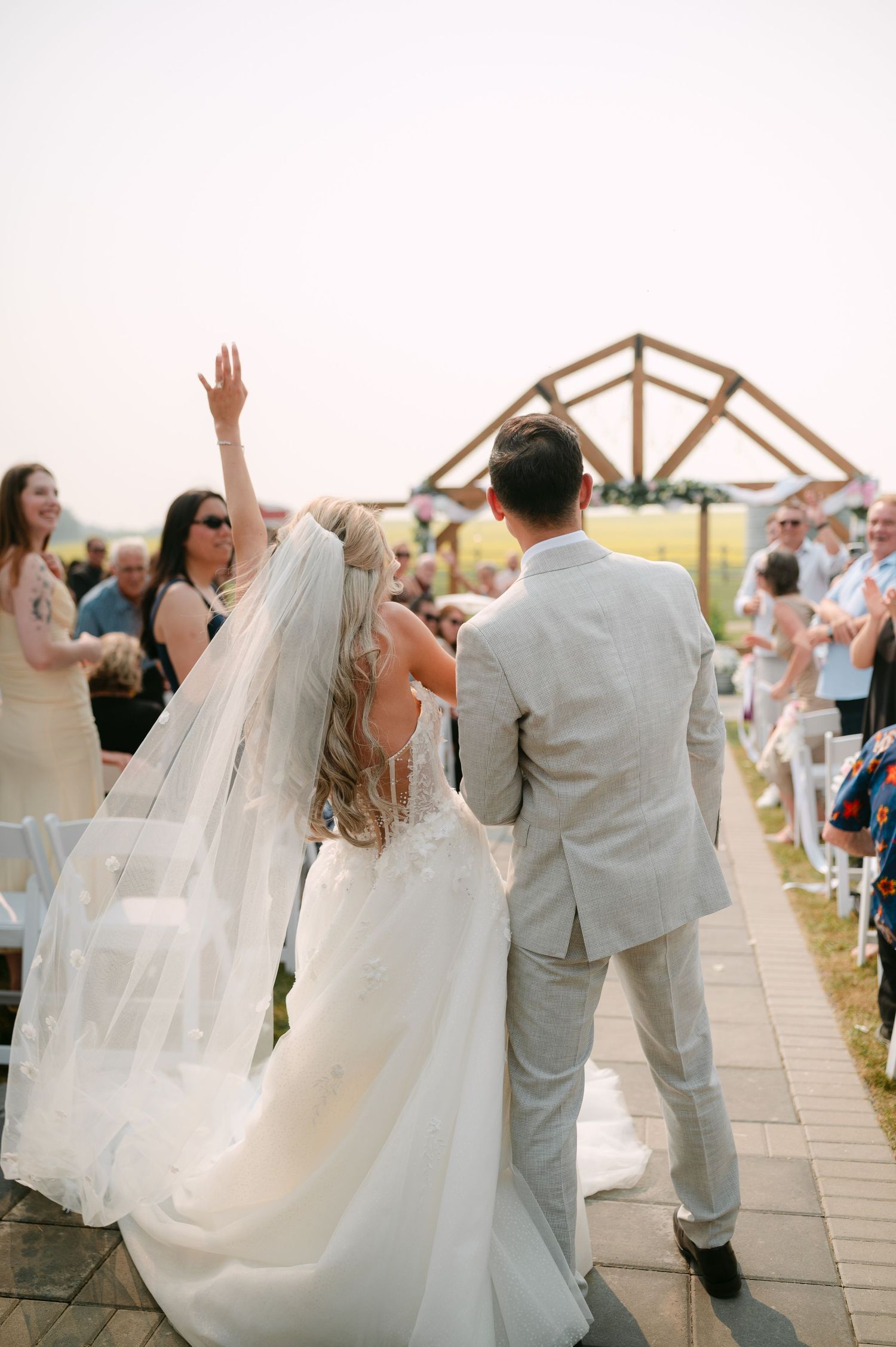 Bride and groom walk back down the aisle after wedding ceremony, bride raising her hand in celebration.