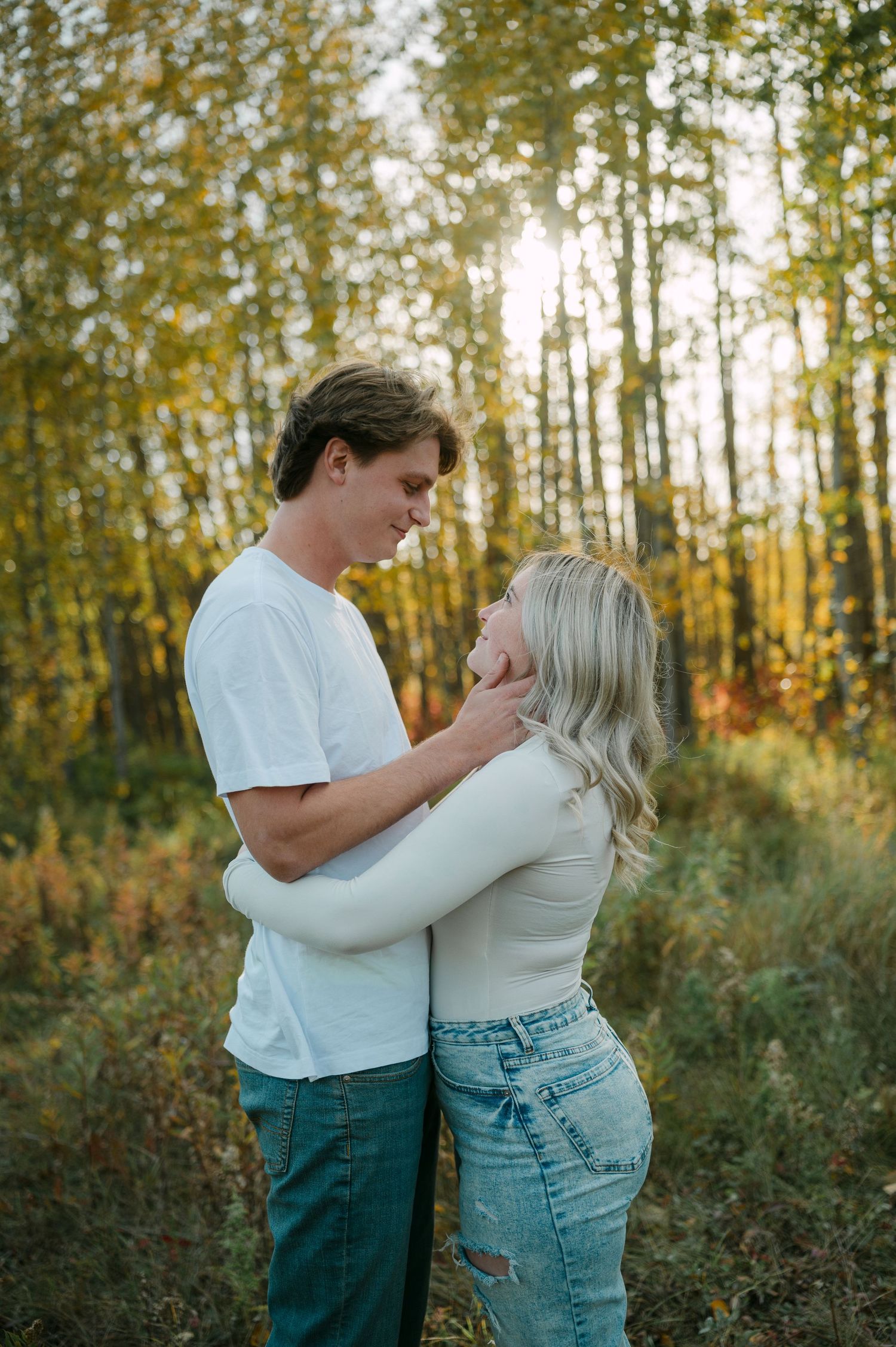 Young couple embracing and gazing at each other in a sunlit autumn forest with golden foliage.