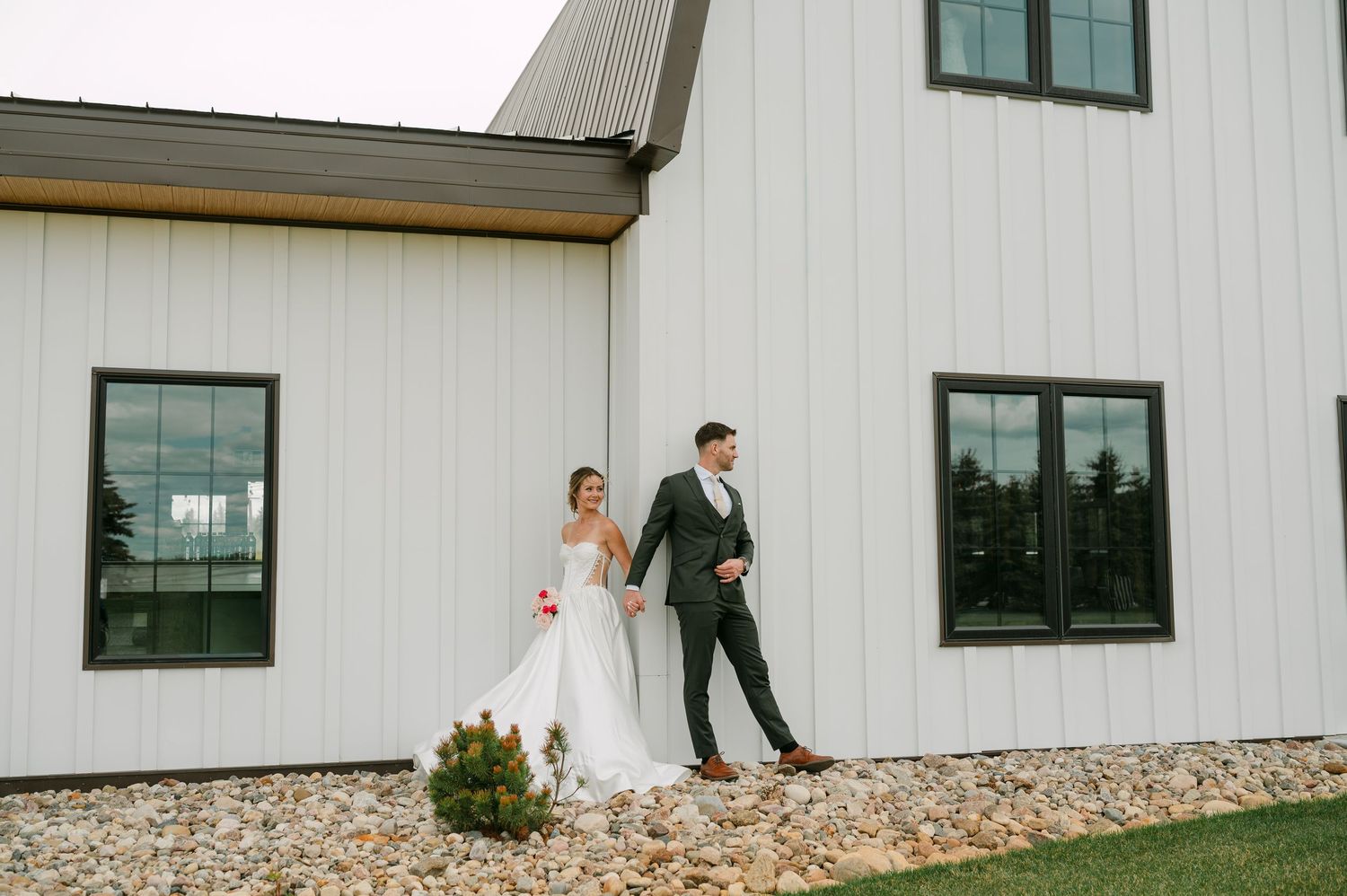 Bride and groom walking hand in hand outside a modern white barn wedding venue.