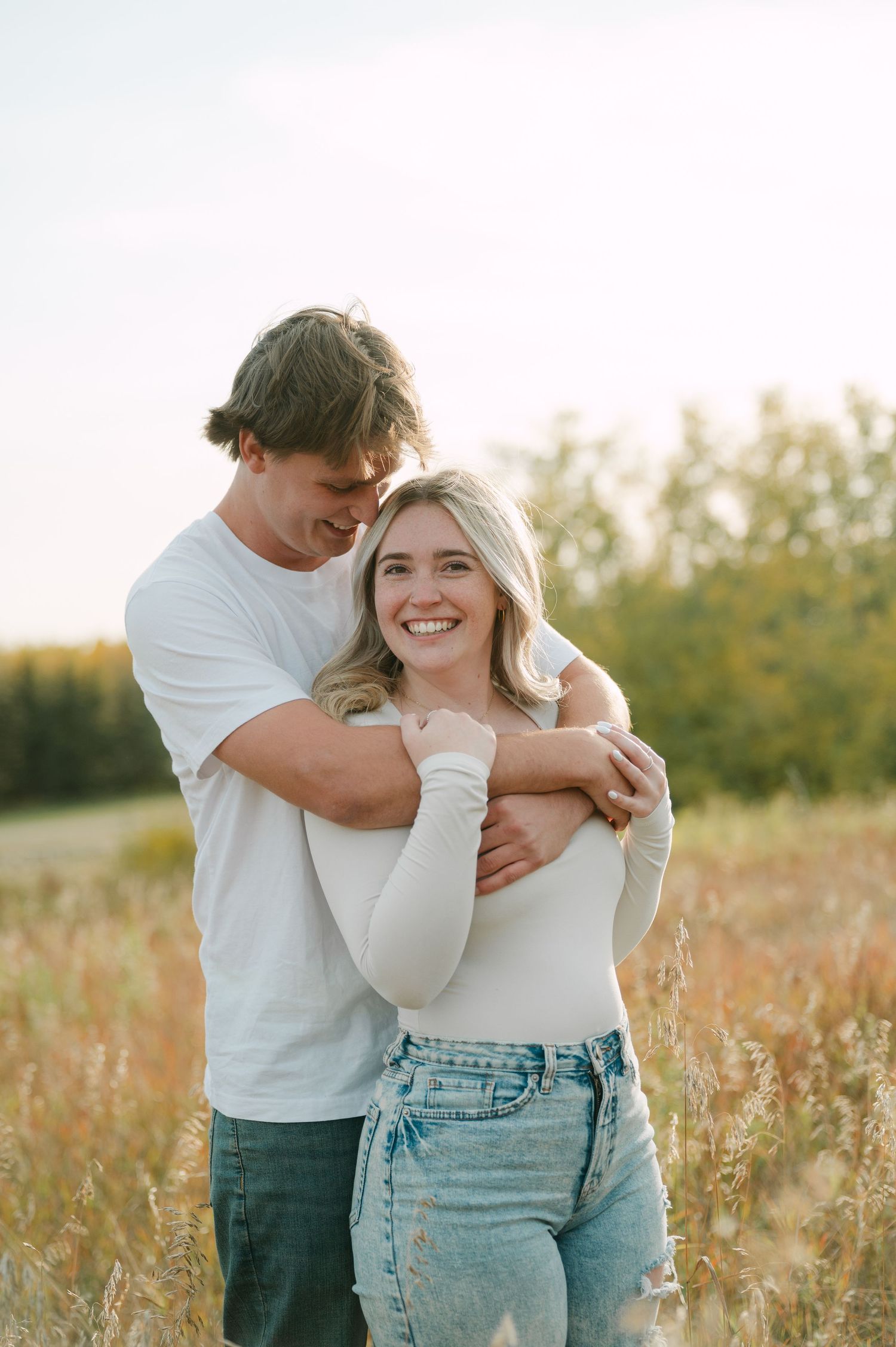 Happy couple embracing in a golden field at sunset, woman smiling brightly at the camera.