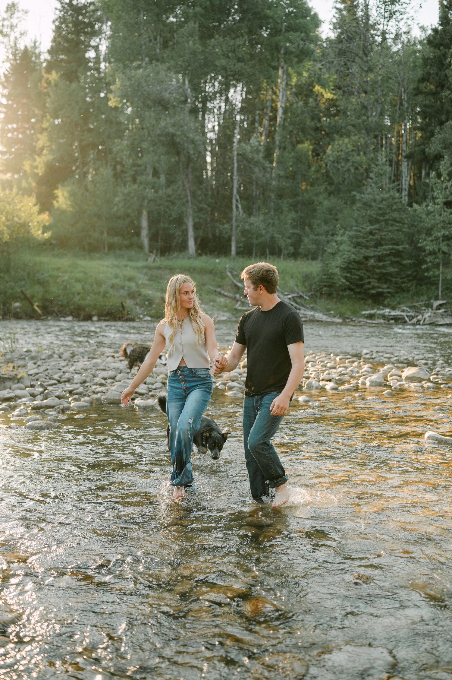 Couple holding hands wading barefoot through a shallow rocky river in a forest. Couples photoshoot