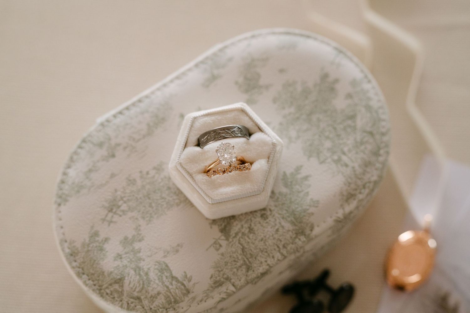 Gold diamond engagement ring and wedding band displayed in a white hexagonal velvet ring box on floral fabric.